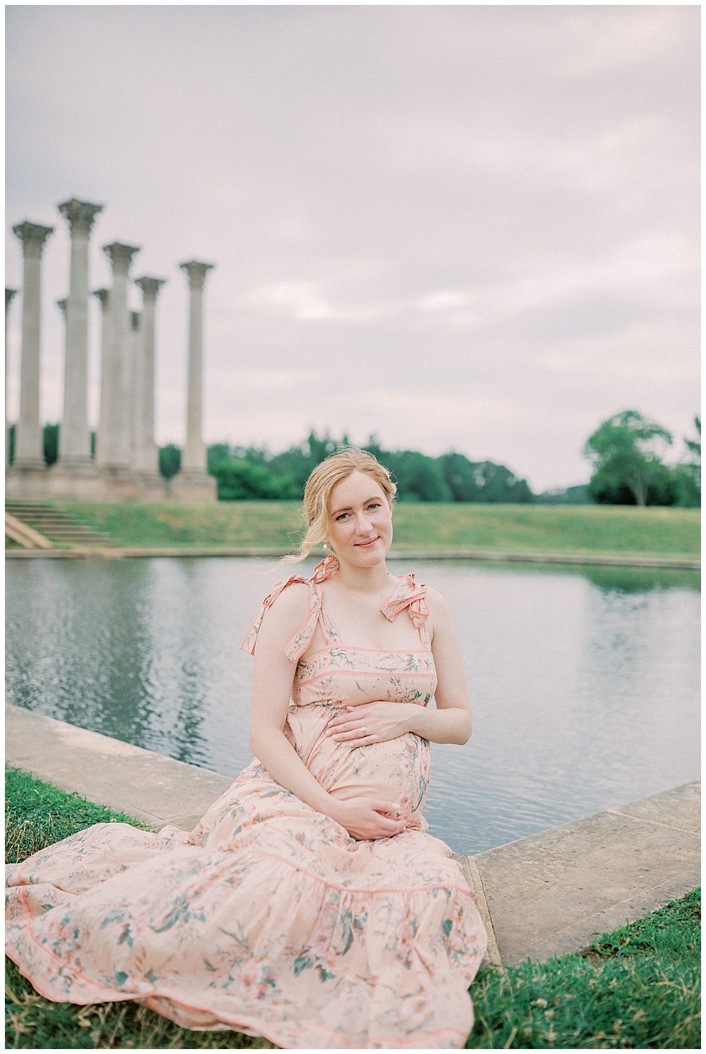 Blonde Pregnant Mother In Pink Dress Sits In Front Of Pond At The National Arboretum.