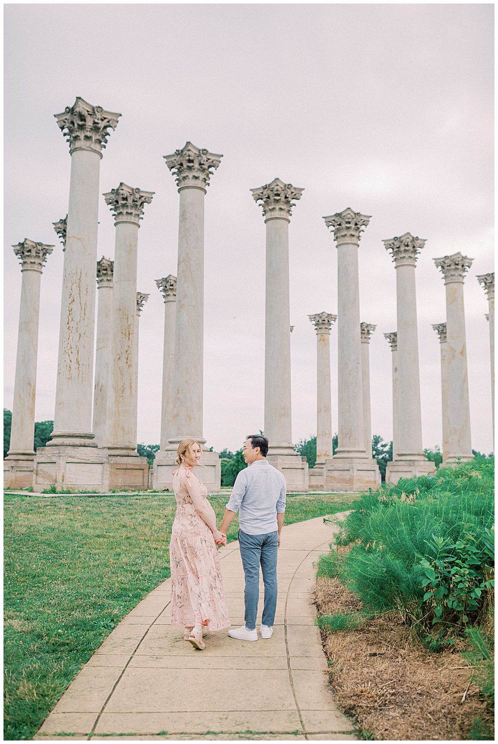 Expecting Parents Walk Up The Sidewalk At The National Arboretum Columns As The Mother Turns Around To Look At The Camera.