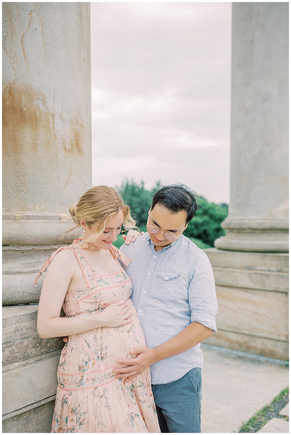 Pregnant Mother Leans Against Pillar While Husband Places Hand On Her Belly During Their National Arboretum Maternity Session.