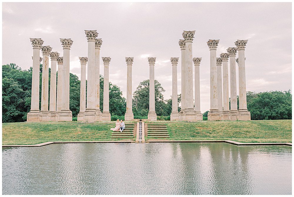 Wide View Of Husband And Wife Sitting On Steps By The Columns At The National Arboretum.