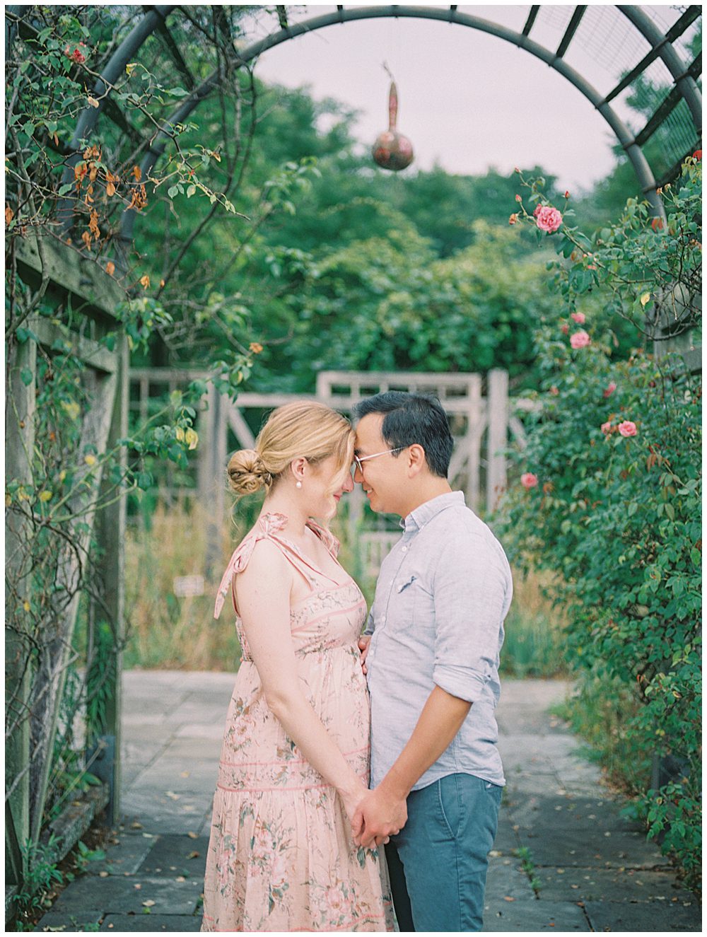 Pregnant Mother Faces Her Husband While Standing Near Rose Bush At The National Arboretum In Dc.