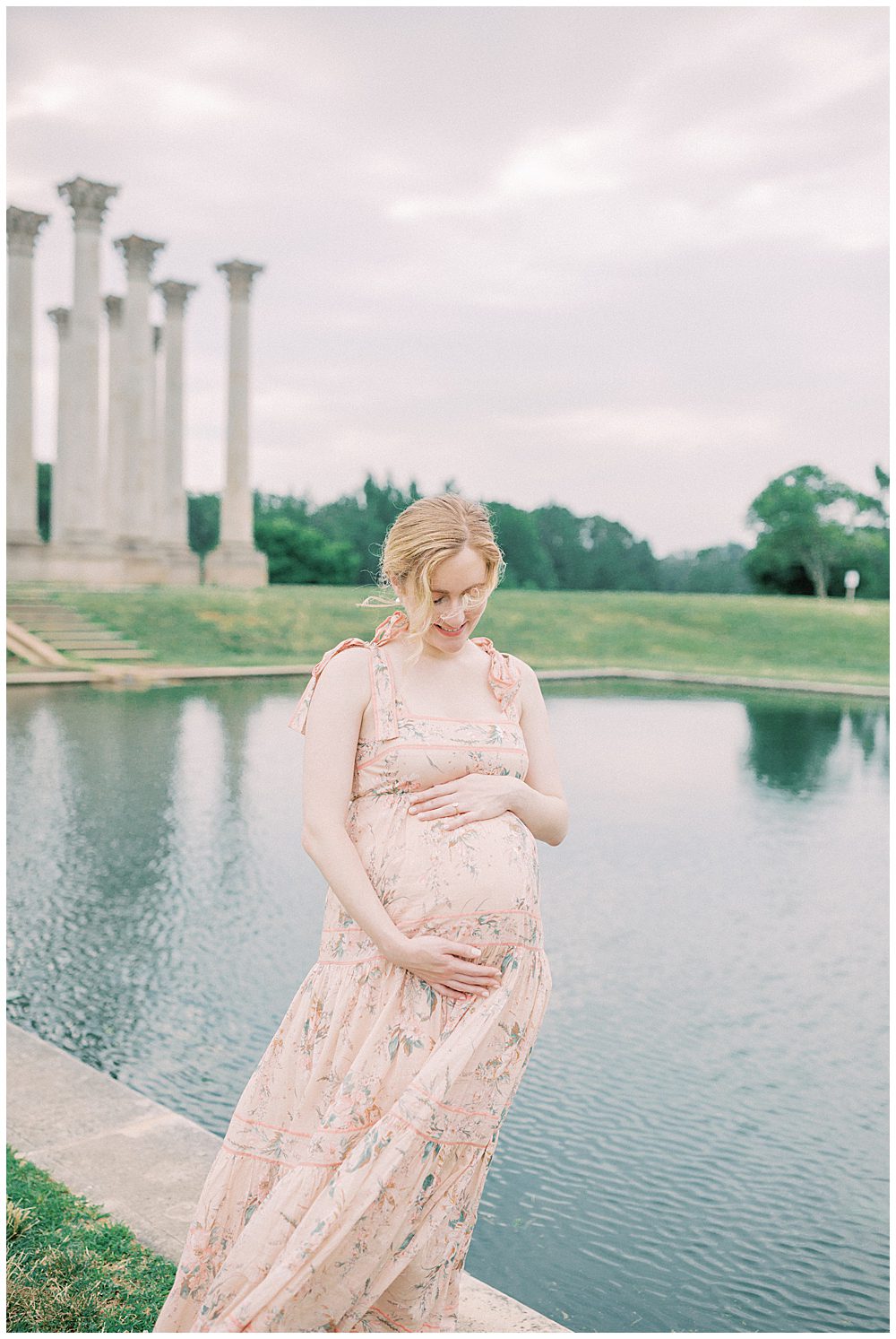 Blonde Pregnant Mother In Pink Zimmerman Dress Stands In Front Of Pond During Her National Arboretum Maternity Session.