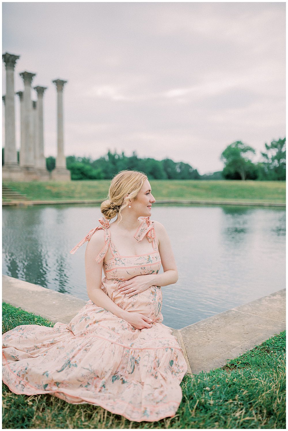 Pregnant Mother Sits In Front Of The Pool At The National Arboretum With Hands On Her Belly, Looking Off Into The Distance.