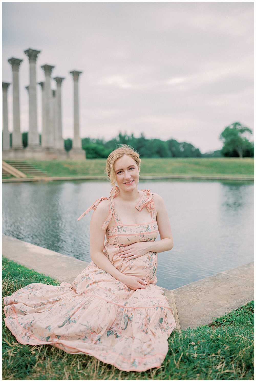 Pregnant Blonde Mother Sits In Front Of Pond At The National Arboretum And Smiles At The Camera.