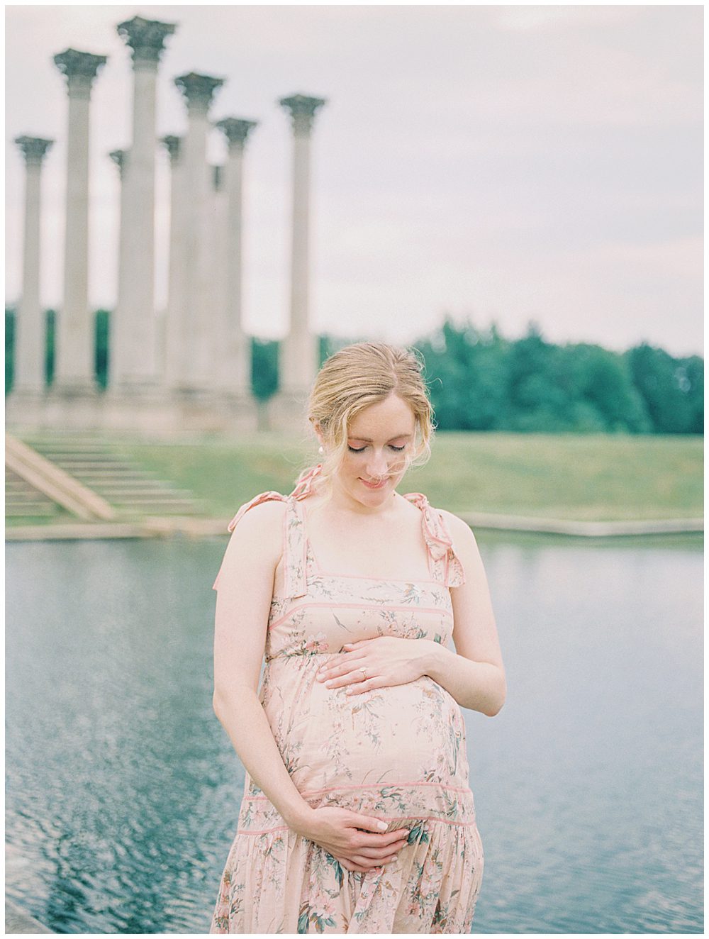 Pregnant Mother Places One Hand On Top And One Hand Below Belly While Standing In Front Of National Arboretum Pond During National Arboretum Maternity Session.