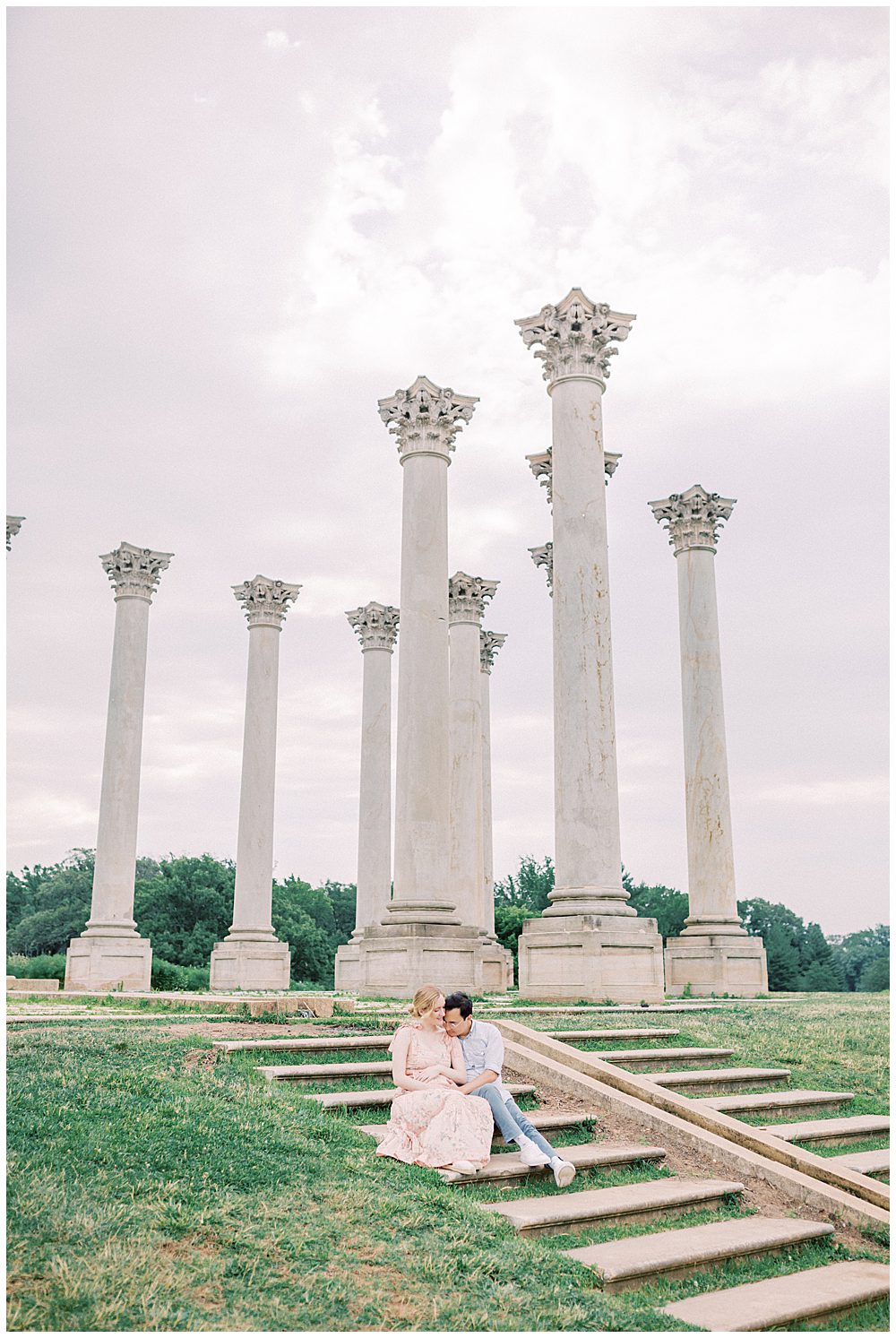 Couple Sits On Steps In Front Of Columns At The National Arboretum During Their National Arboretum Maternity Session.