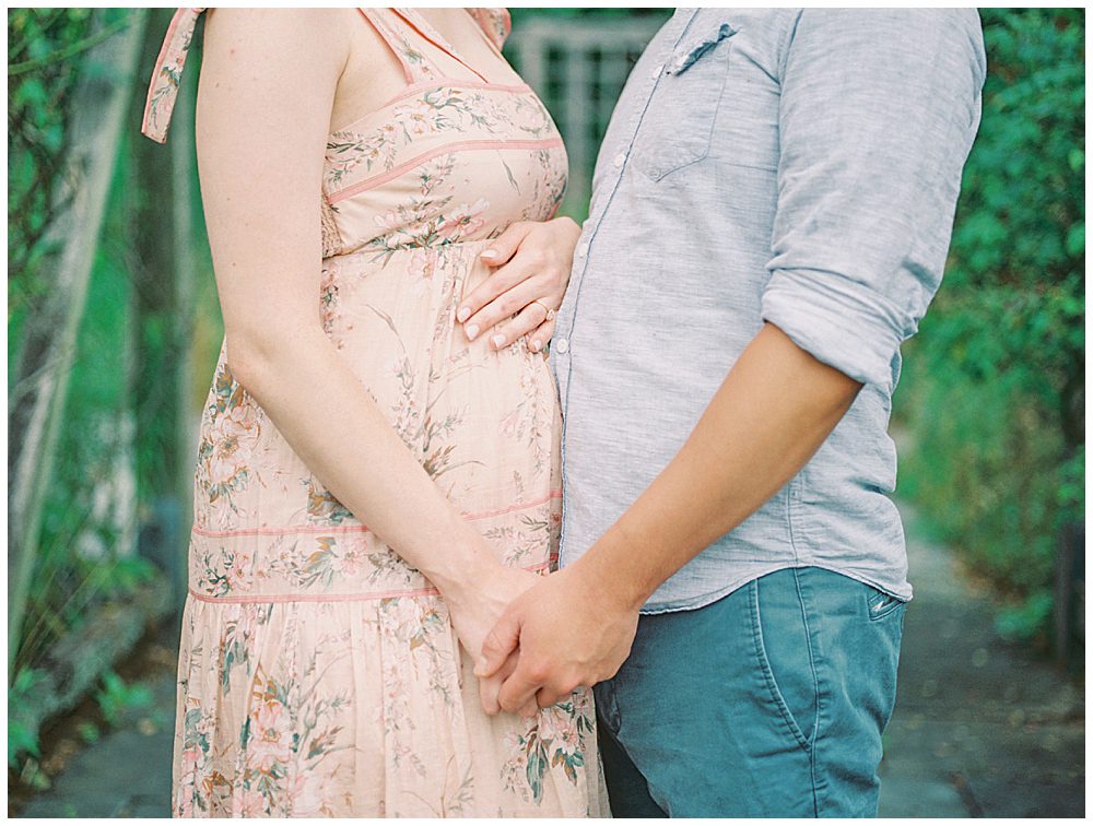 Husband And Wife Hold Hands During Their Maternity Session.