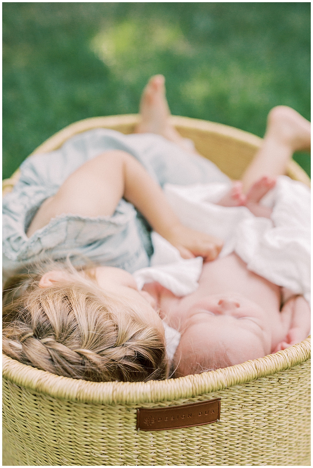 Toddler Girl Lays In Moses Basket With Her Baby Sister