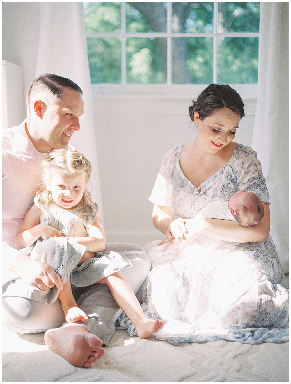 Mother Holds Newborn Baby While Dad Holds Toddler Girl On His Lap During Newborn Session