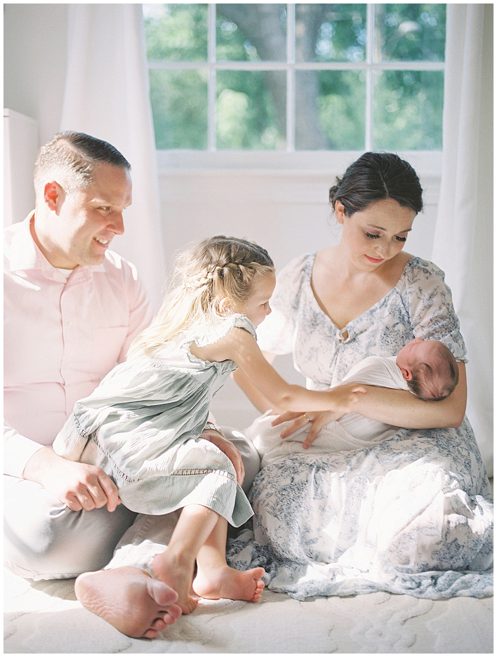 Toddler Girl Leans Over And Touches Her Newborn Sister During A Newborn Session