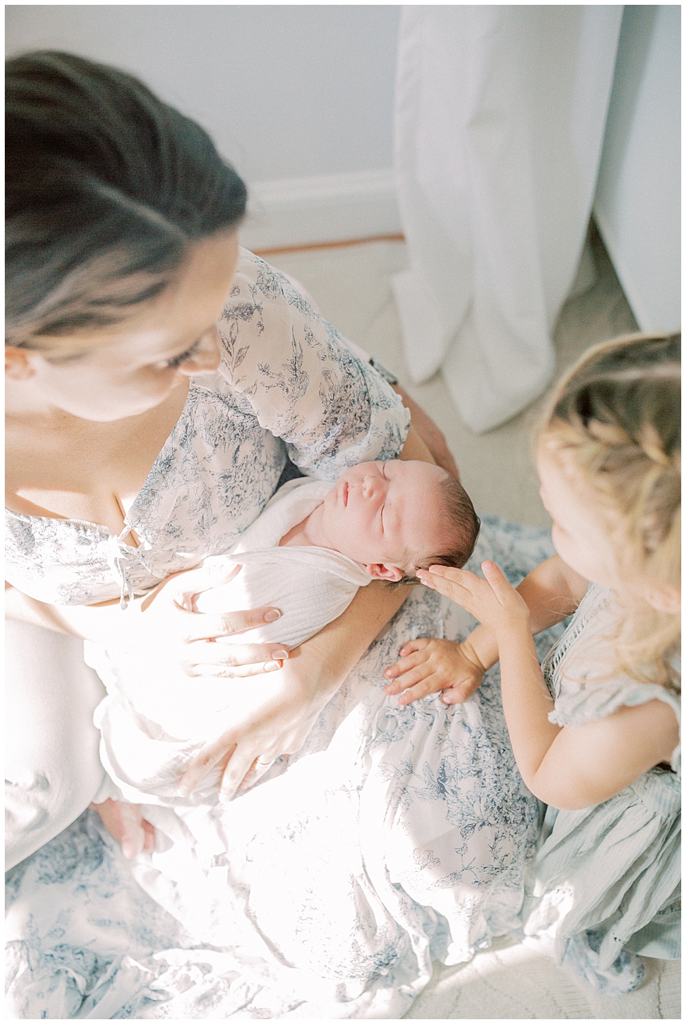 Toddler Girl Touches Her Baby Sister's Head While Baby Is Held By Her Mother