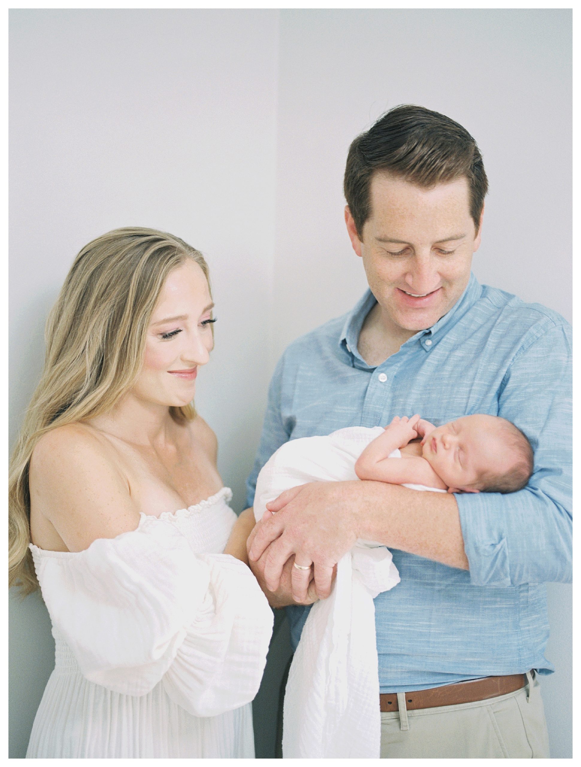 Father Holds His Newborn Baby While Mother Stands Next To Him 