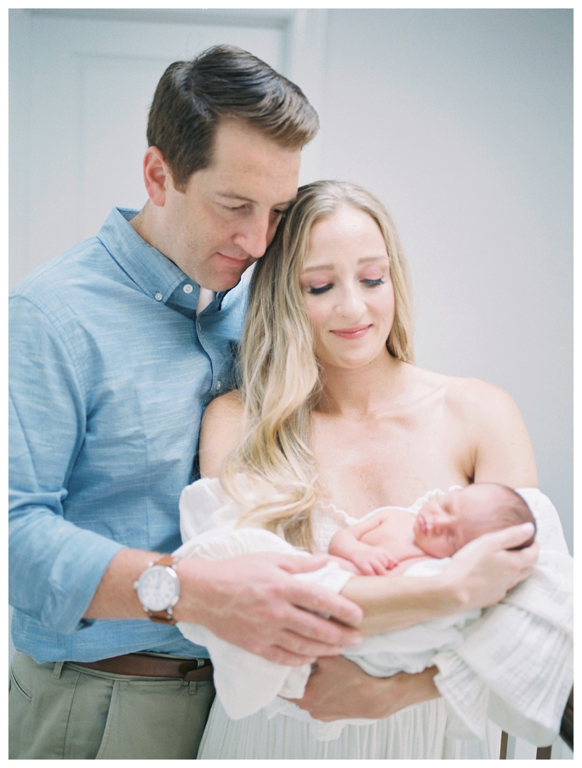 Mother And Father Stand Together Holding Newborn Baby During Newborn Session.