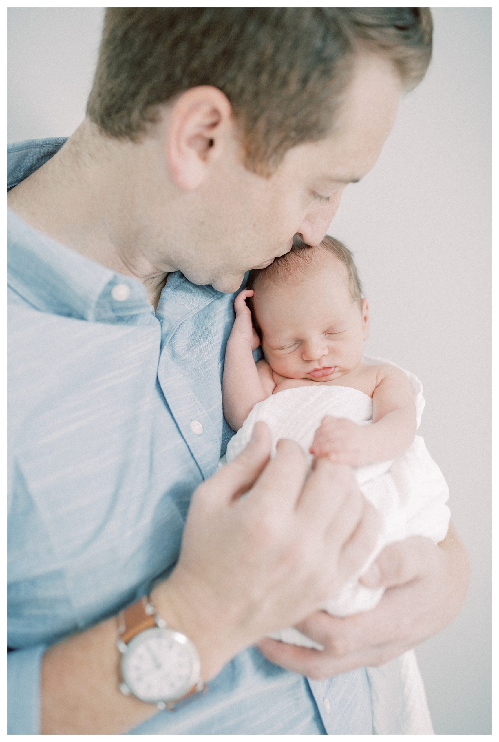 Father Leans Down And Kisses His Newborn On The Head.