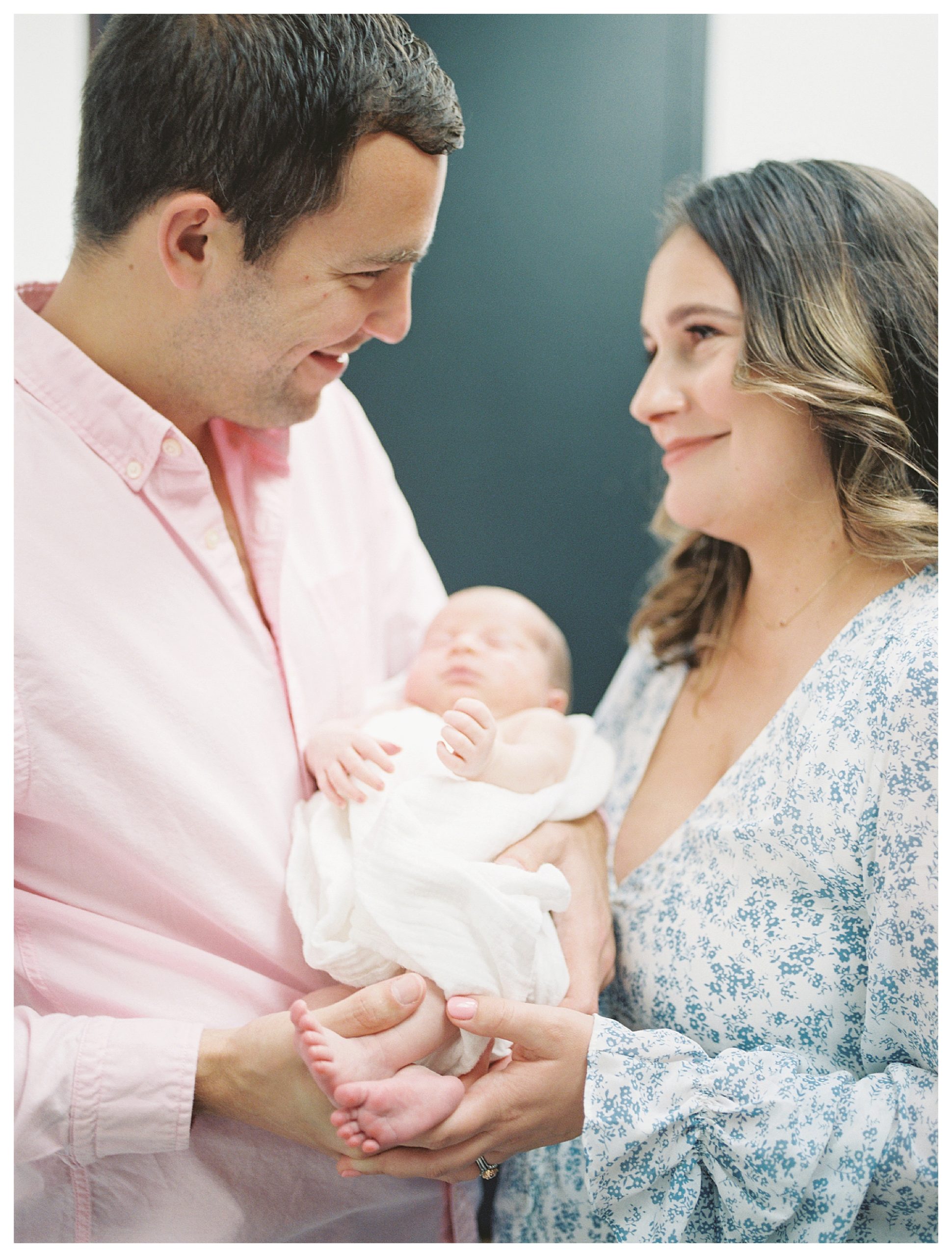 New Parents Face And Smile At One Another As They Hold Their Newborn Baby Girl