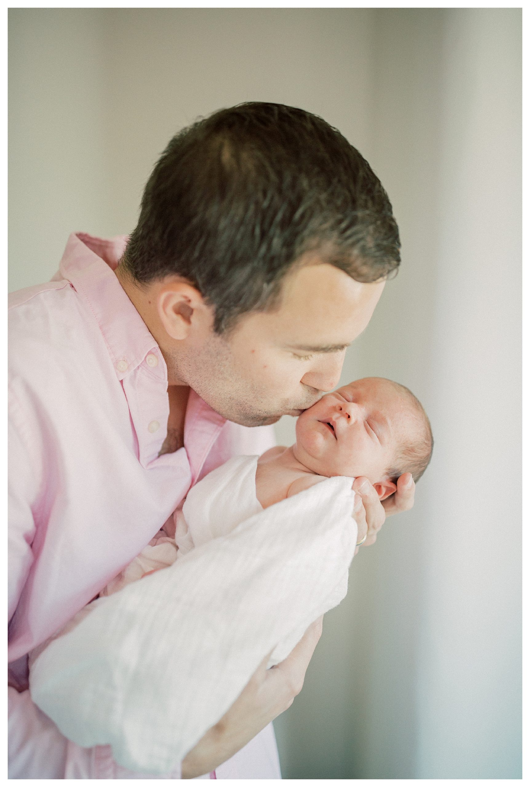 Father Kisses His Newborn Baby Girl's Cheek During In-Home Newborn Session.