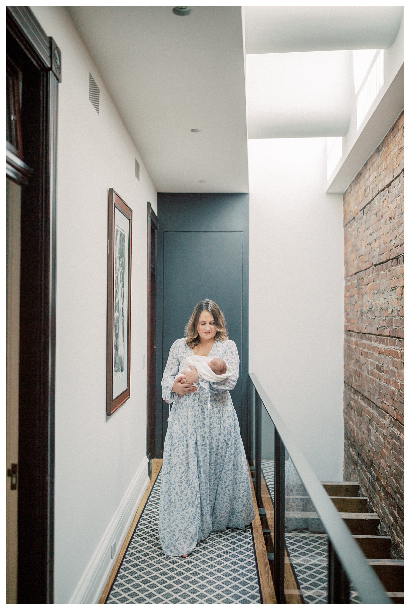 Mother Walks In Hallway, Looking Down At Her Newborn Baby During In-Home Newborn Session