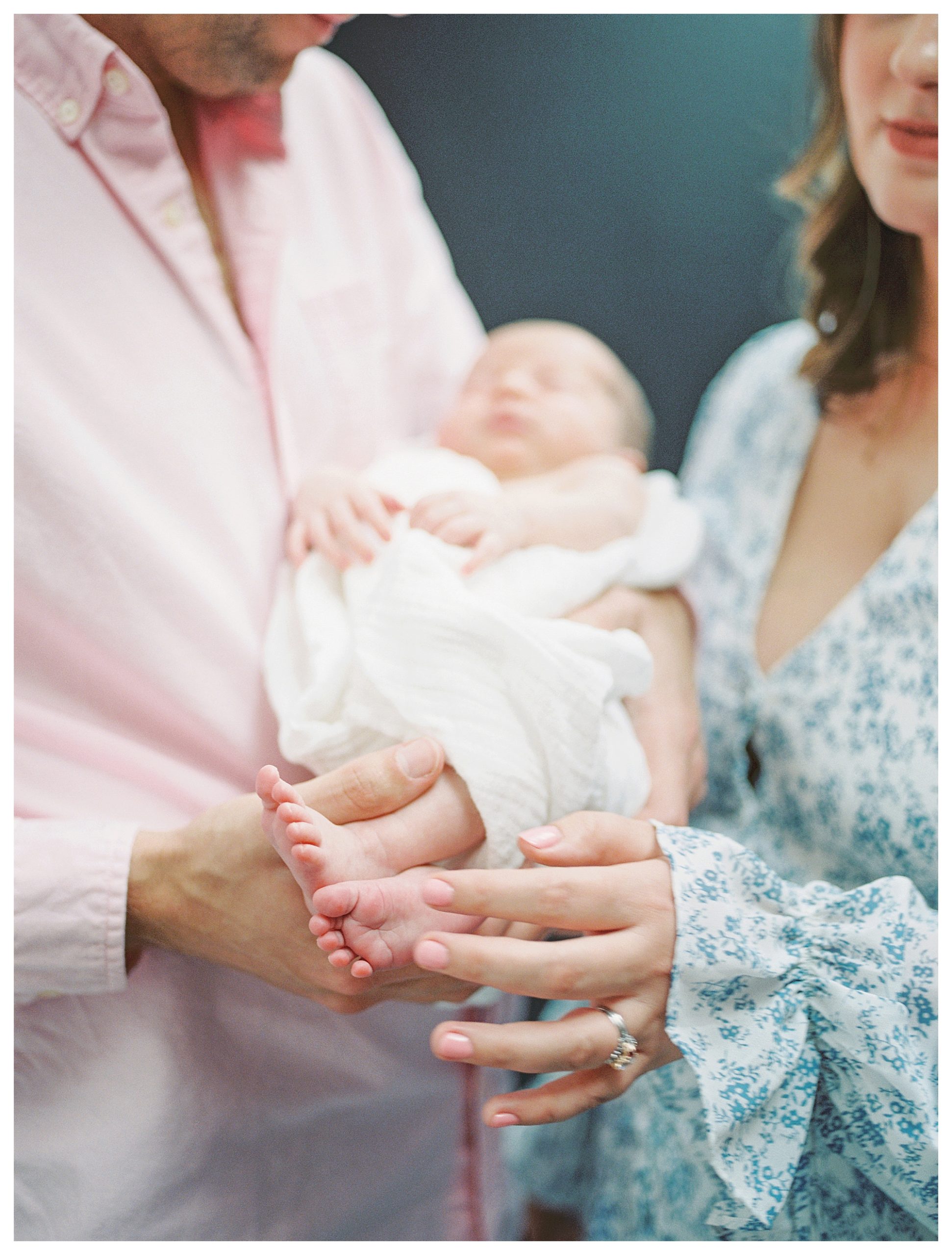 New Parents Hold Infant Baby And Mom Gently Touches Baby's Feet During In-Home Newborn Session.