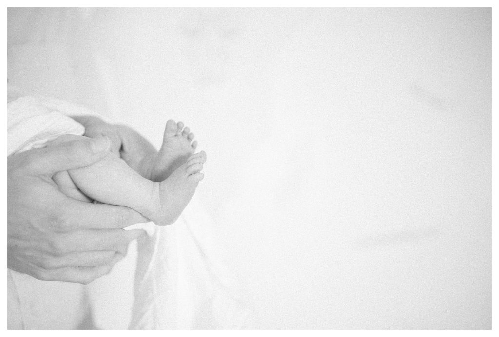 Close-Up View Of Father Holding Baby's Legs During In-Home Newborn Session