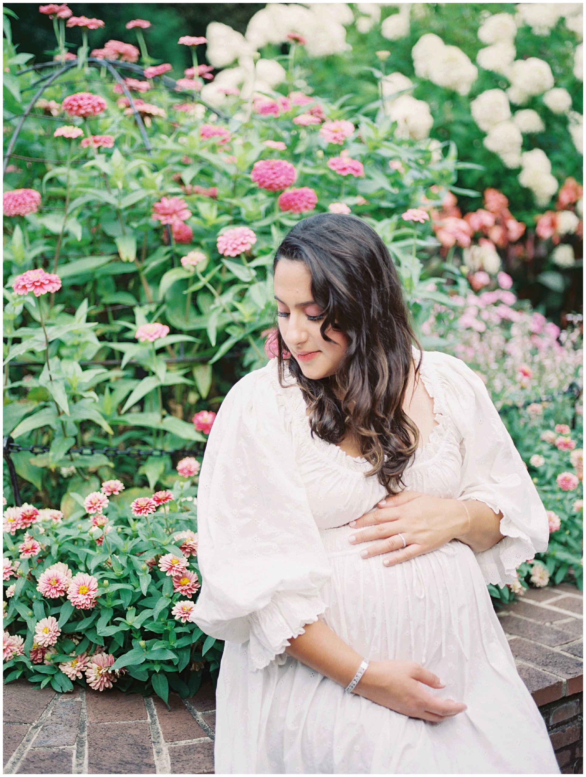 Pregnant Mother Sits On A Brick Wall In Front Of Pink Flowers At Brookside Gardens.