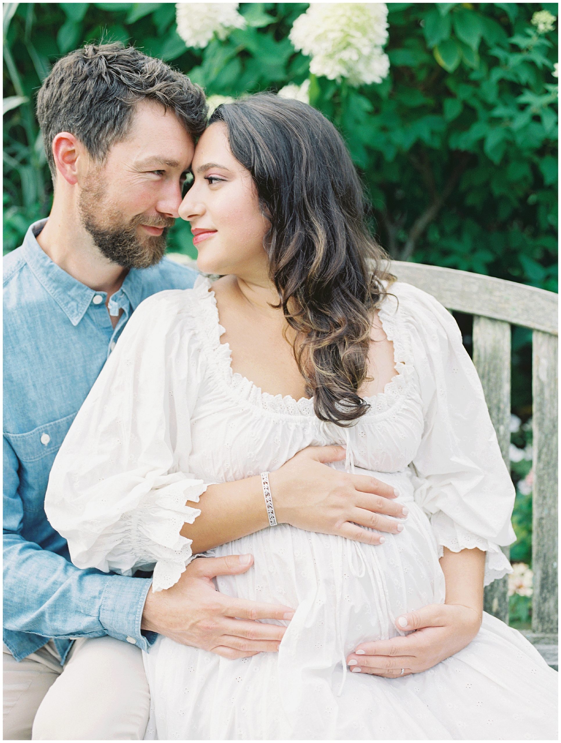 Pregnant Mother Leans Into Her Husband While Sitting On A Bench In Brookside Gardens.