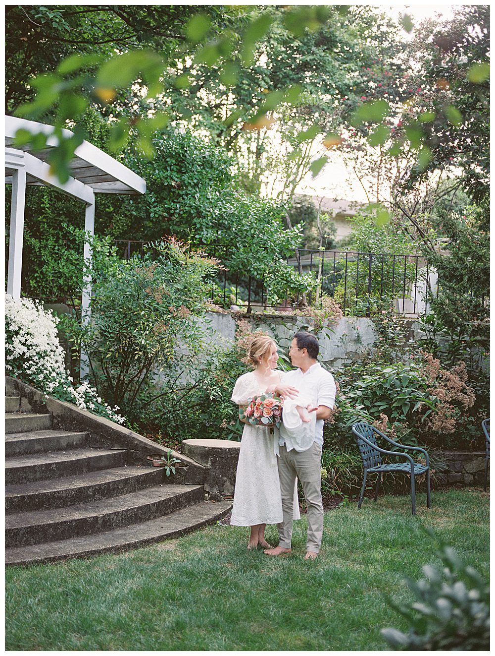 Parents Smile At One Another While Holding Their Baby And Bouquet Of Roses During Alexandria Va Newborn Session.