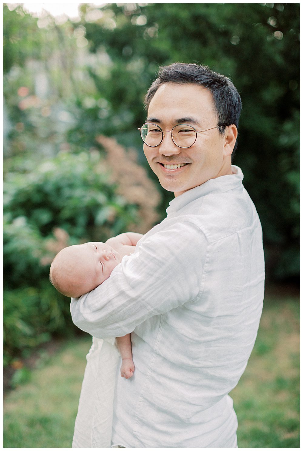 Dad Smiles At Camera While Holding Newborn Baby.