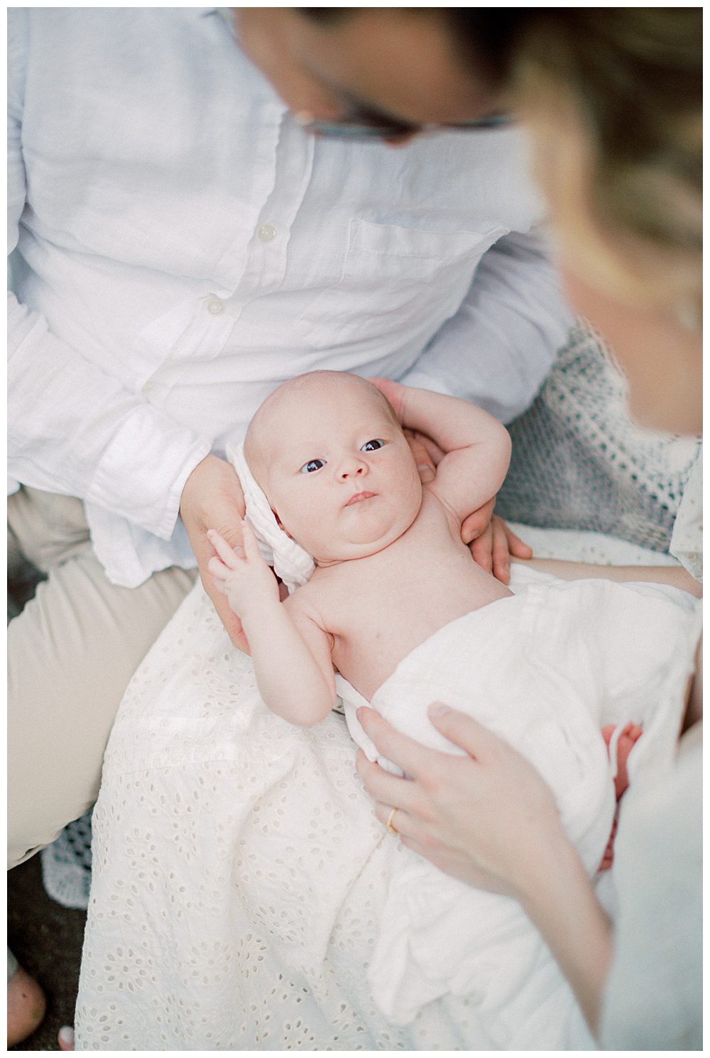 Baby Held In Her Parents' Laps During Outdoor Newborn Session.