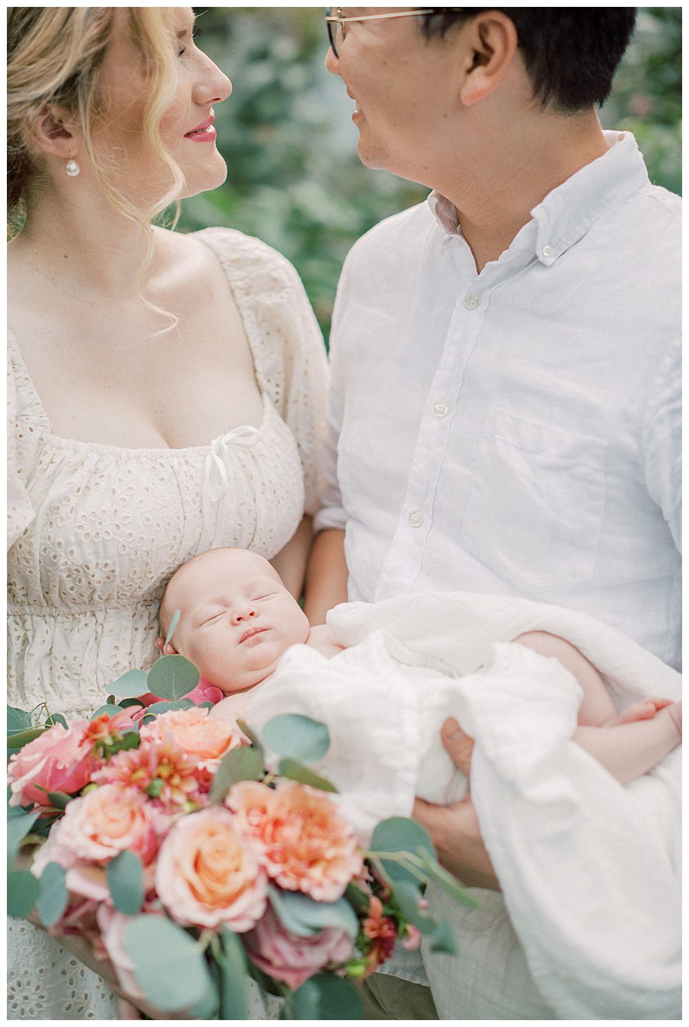 Newborn Baby Sleeps Peacefully While Being Held By Parents.