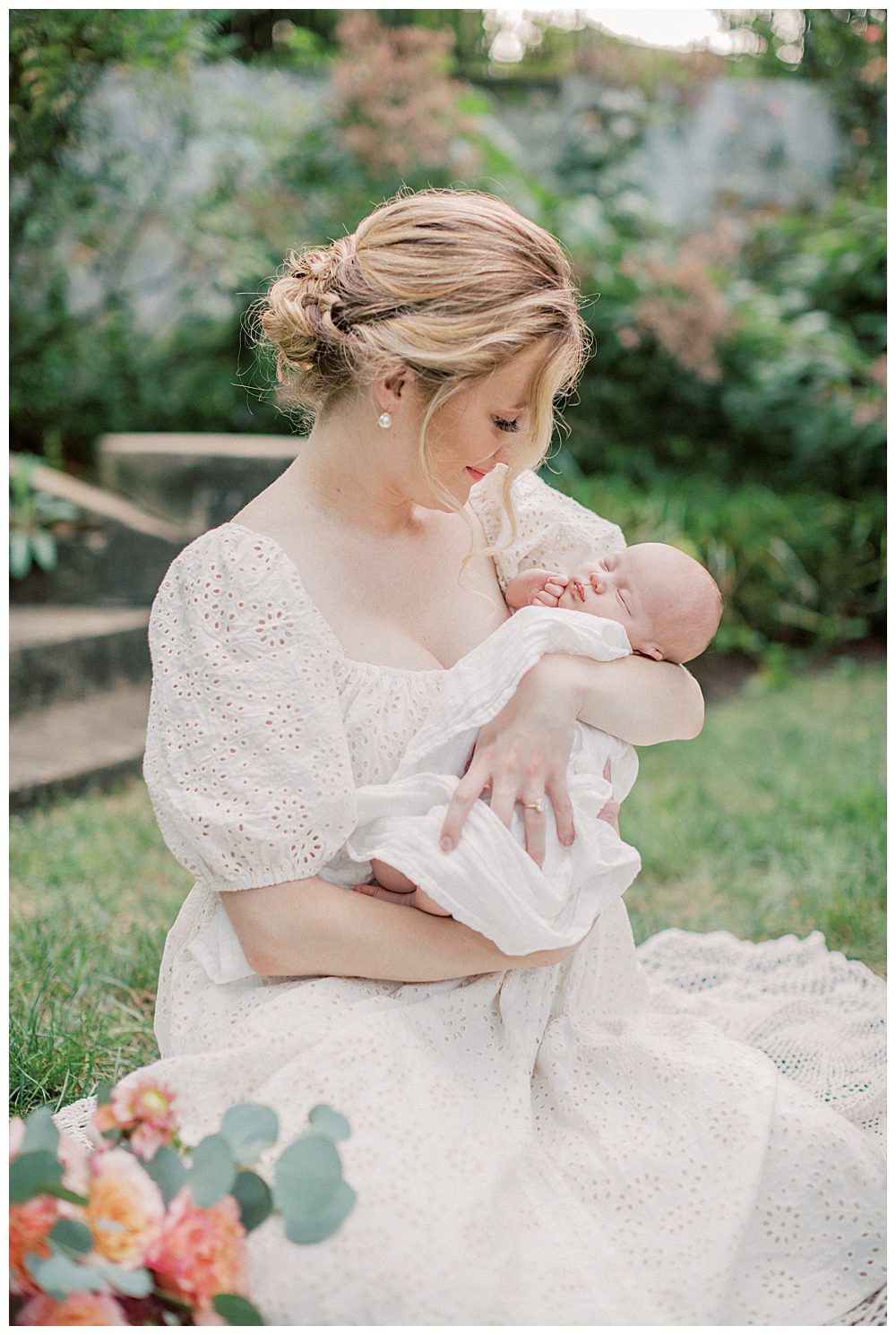 Mother Smiles Down At Her Newborn Daughter While Sitting On Crochet Blanket Outside.