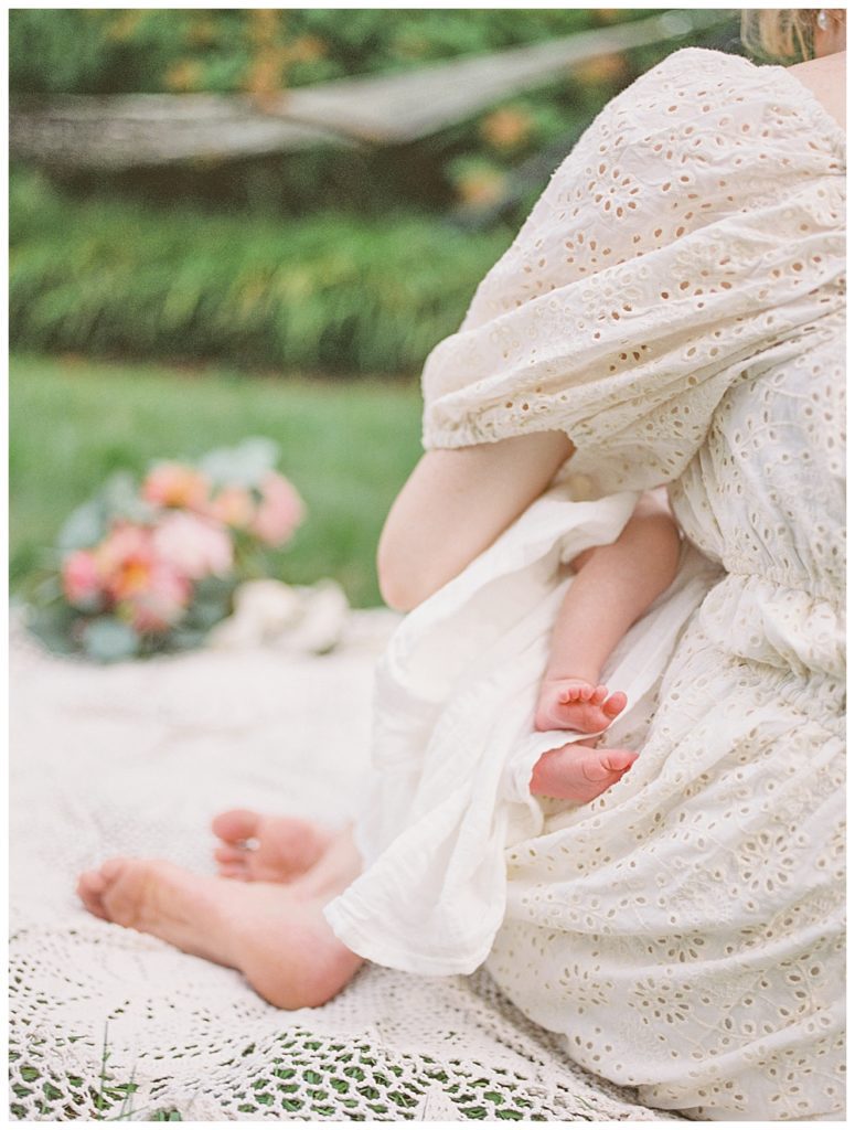 Baby Toes Sticking Out Of A Mother's Arms As She Sits On The Ground.