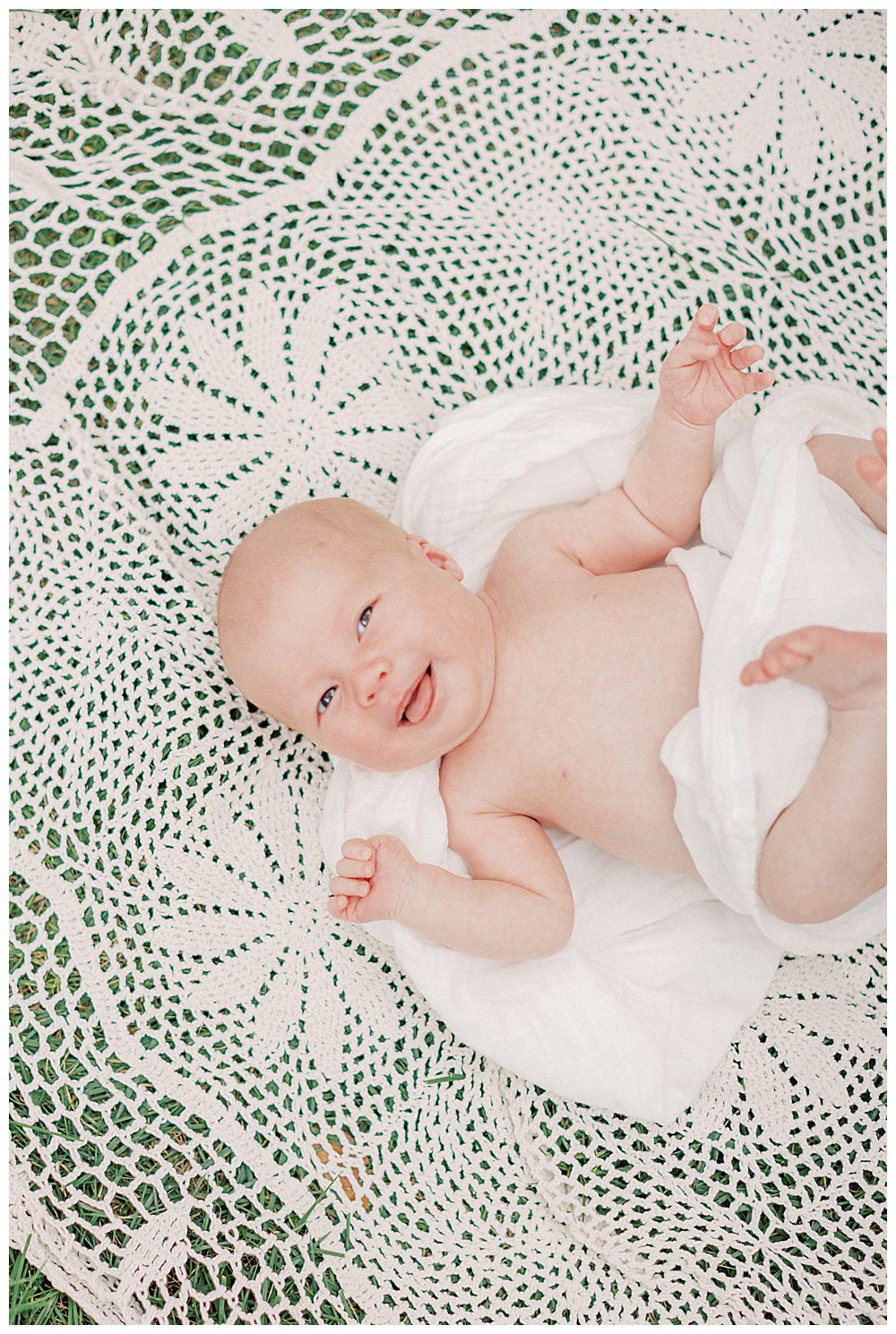 Newborn Baby Girl Smiles As She Lays On Crochet Blanket Outside.