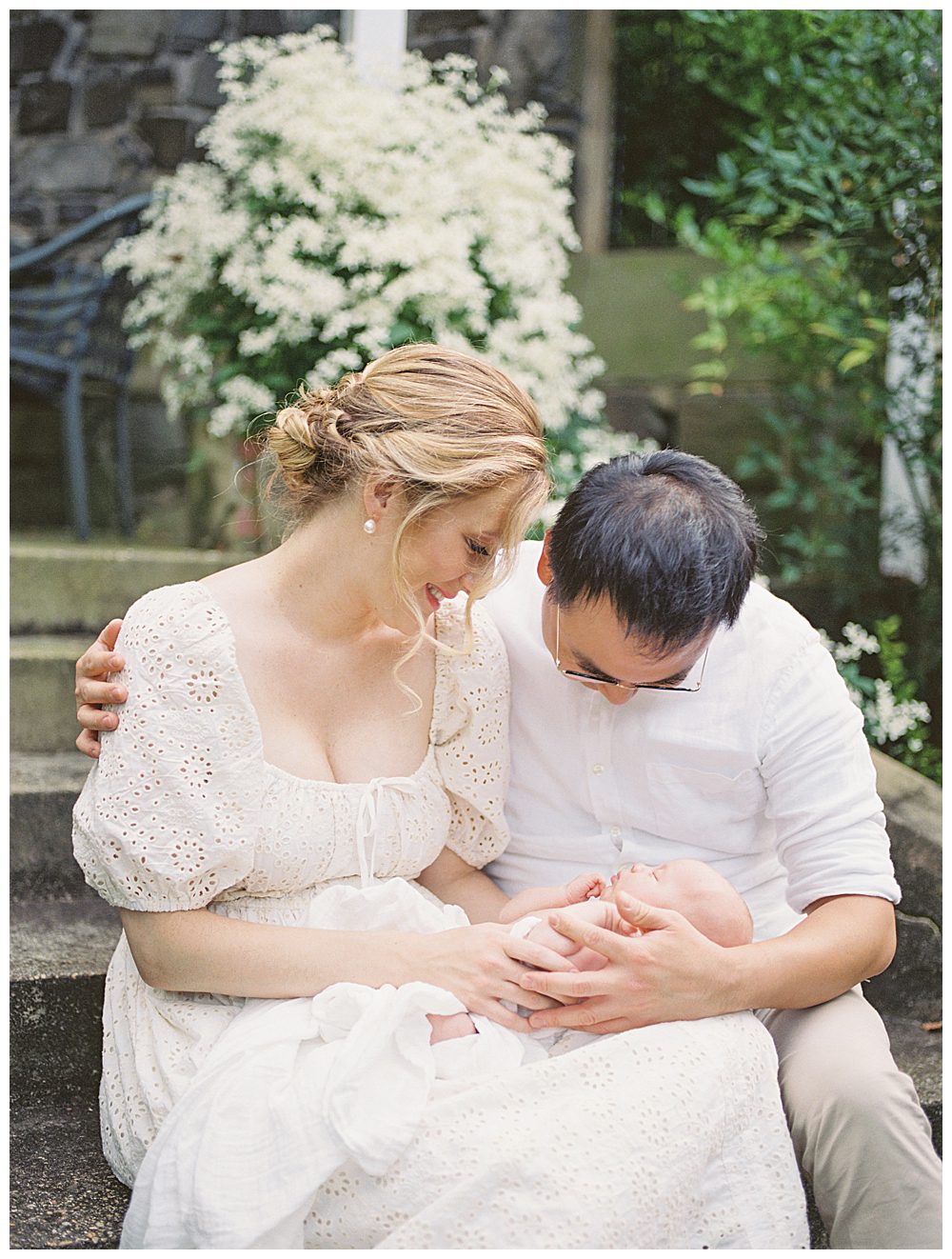 Mother And Father Hold And Smile Down At Newborn Baby Girl During Alexandria Va Newborn Session.