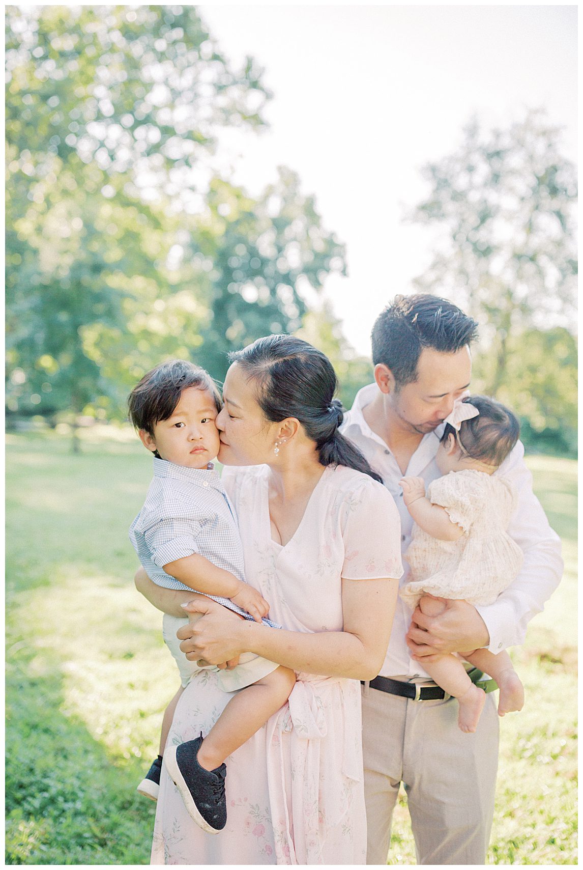 Mother Holds Her Son While Kissing His Cheek With Father Holding Infant Daughter At Colvin Run Mill.