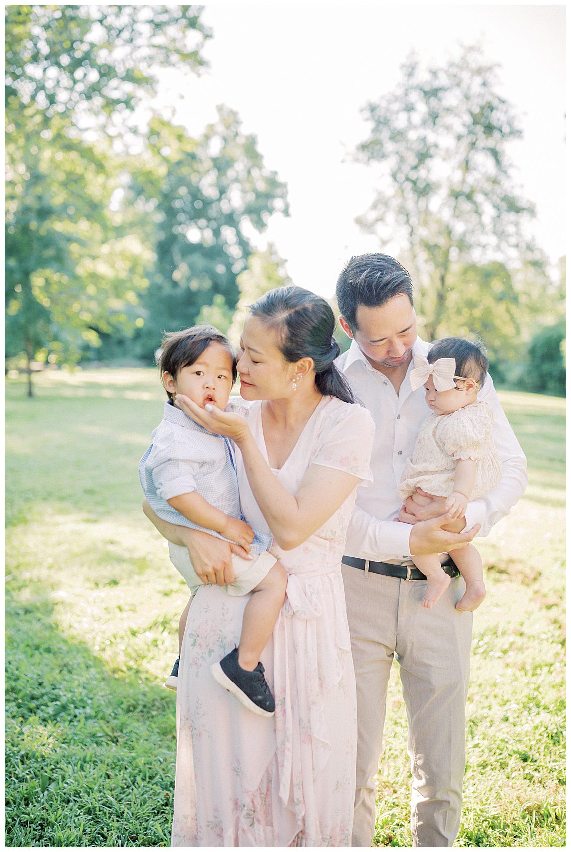 Mother And Father Hold Their Two Children In Green Pasture At Colvin Run Mill.