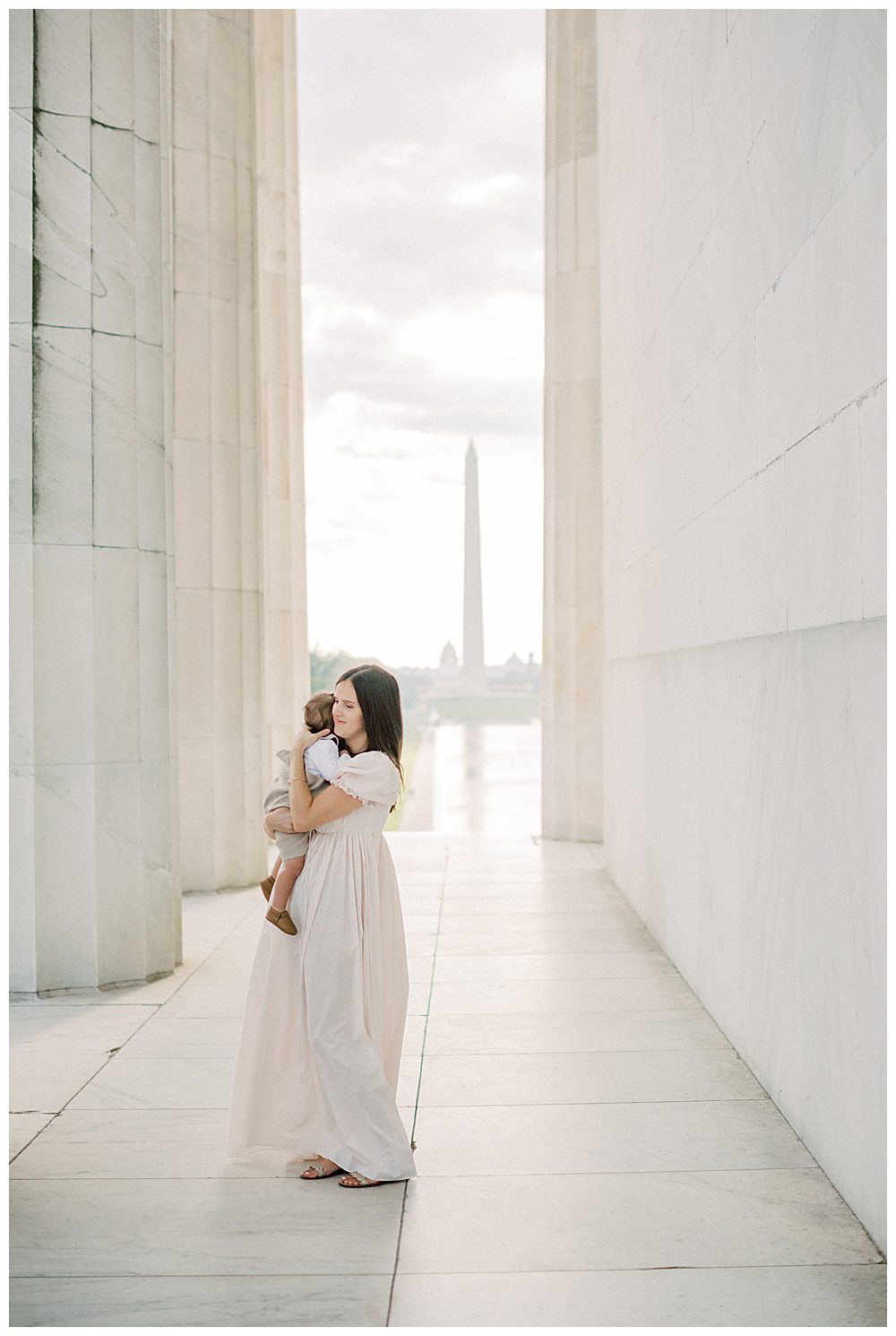 Mother In Pink Selkie Dress Holds Toddler Son While Standing In The Lincoln Memorial During Dc Monuments Family Photo Session.