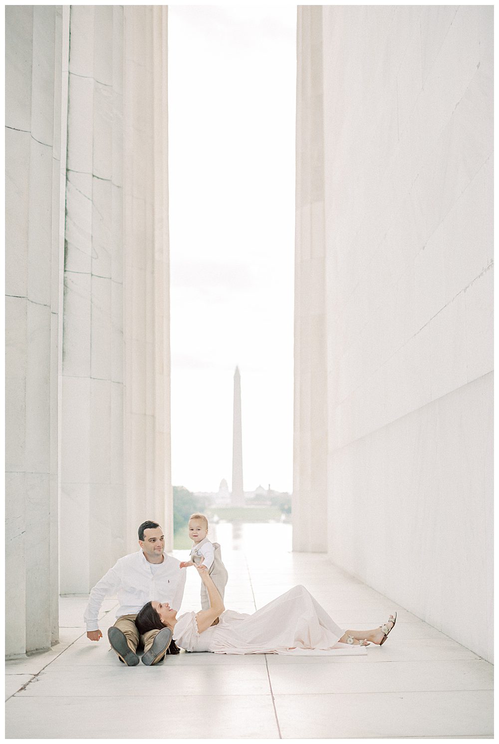 Mother Lays In Her Husband's Lap As She Holds Up Her Toddler Son At The Lincoln Memorial During Dc Monuments Family Photo Session.