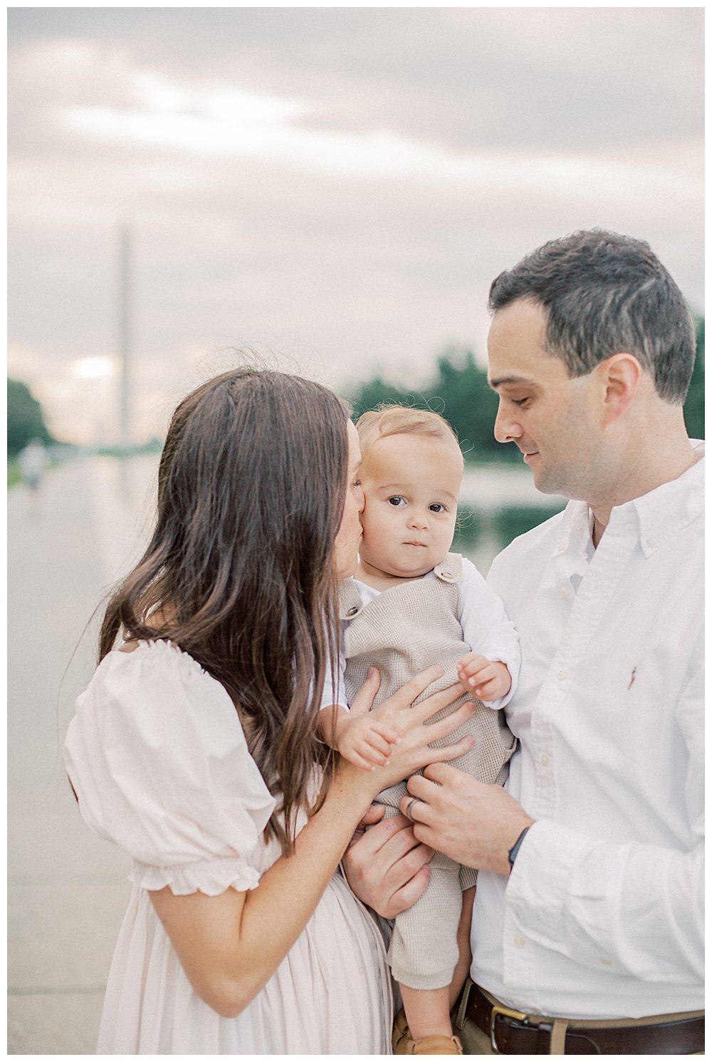 Mother Kisses Toddler's Cheek While Being Held By His Father During Dc Monuments Family Photo Session.