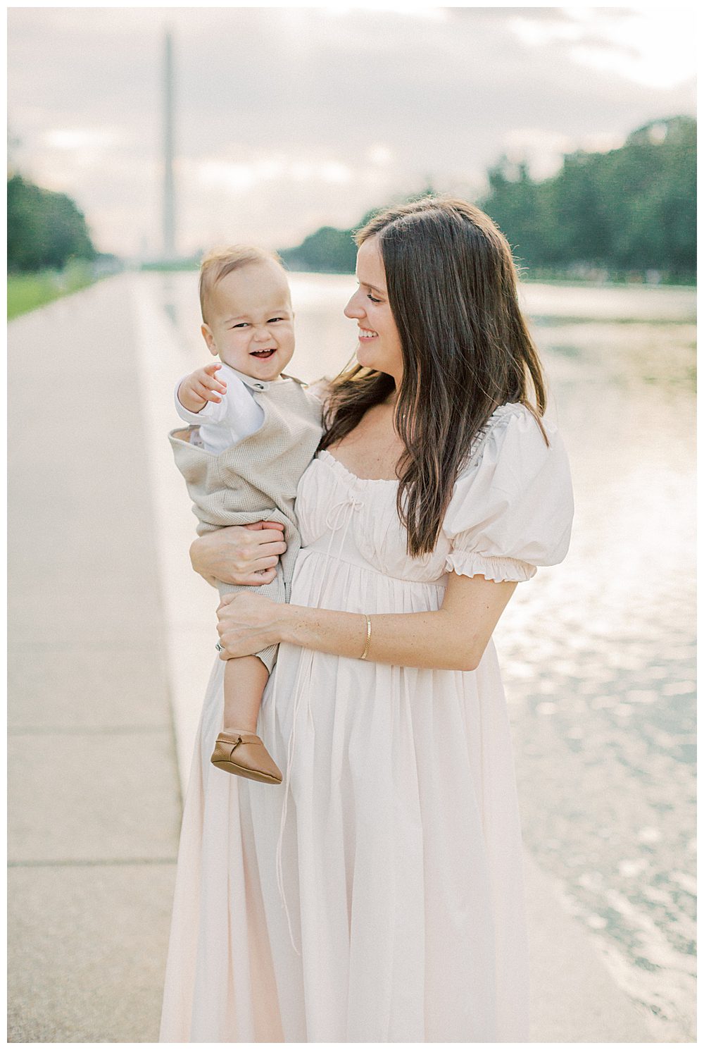 Mother Smiles At Her Toddler Son While Holding Him In Front Of The Reflecting Pool In Washington Dc.