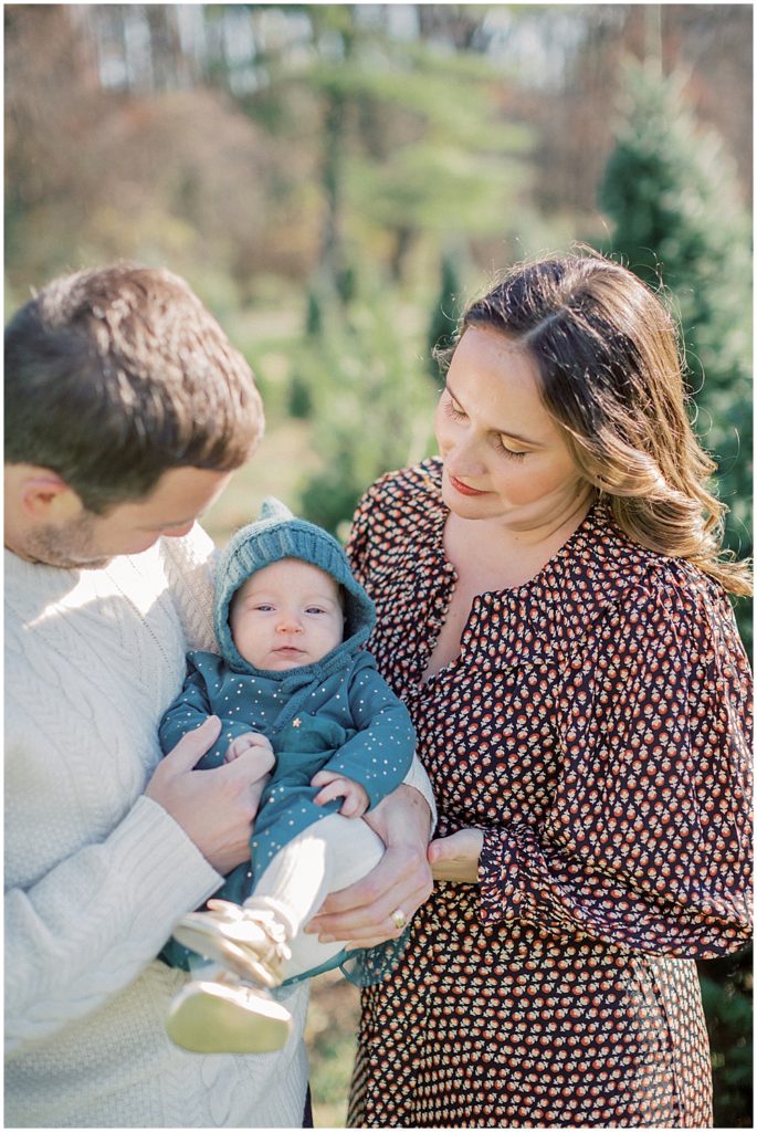 Parents Look Down At Their Infant Daughter During Christmas Mini Sessions At Butler's Orchard.