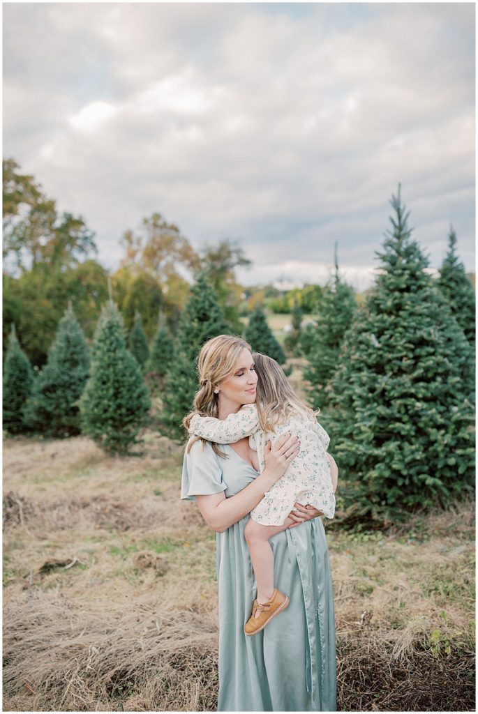 Mom Closes Eyes As She Holds Her Toddler Daughter During Christmas Tree Farm Mini Sessions At Butler's Orchard.