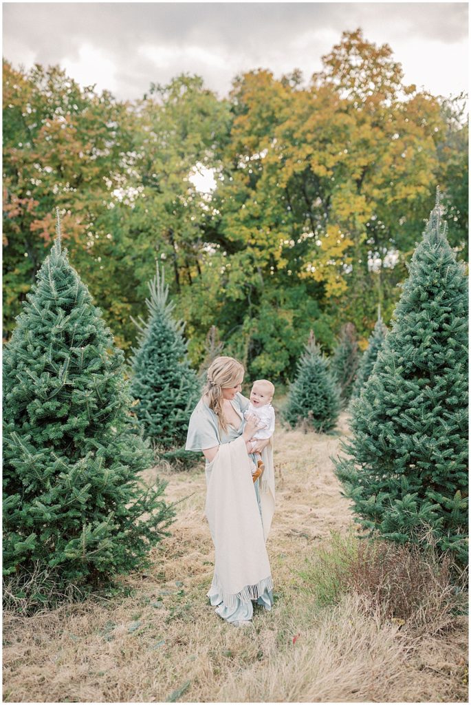 Mom Smiles While Holding Infant Daughter At Butler's Orchard Christmas Tree Farm.