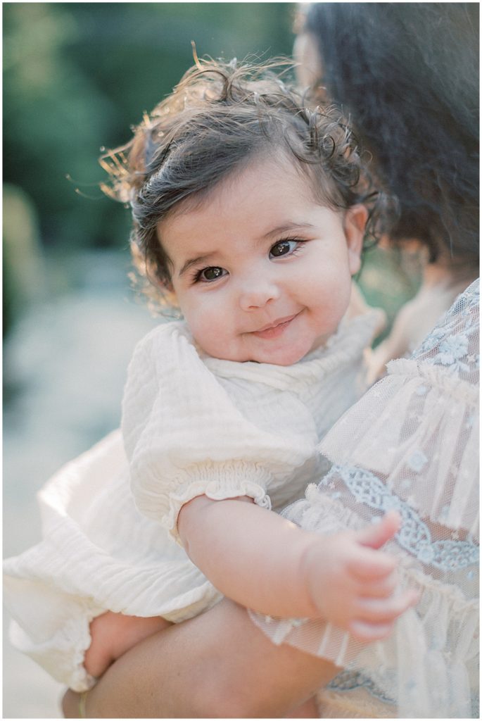 Brown-Eyed Baby Girl Smiles While Being Held By Her Mother.