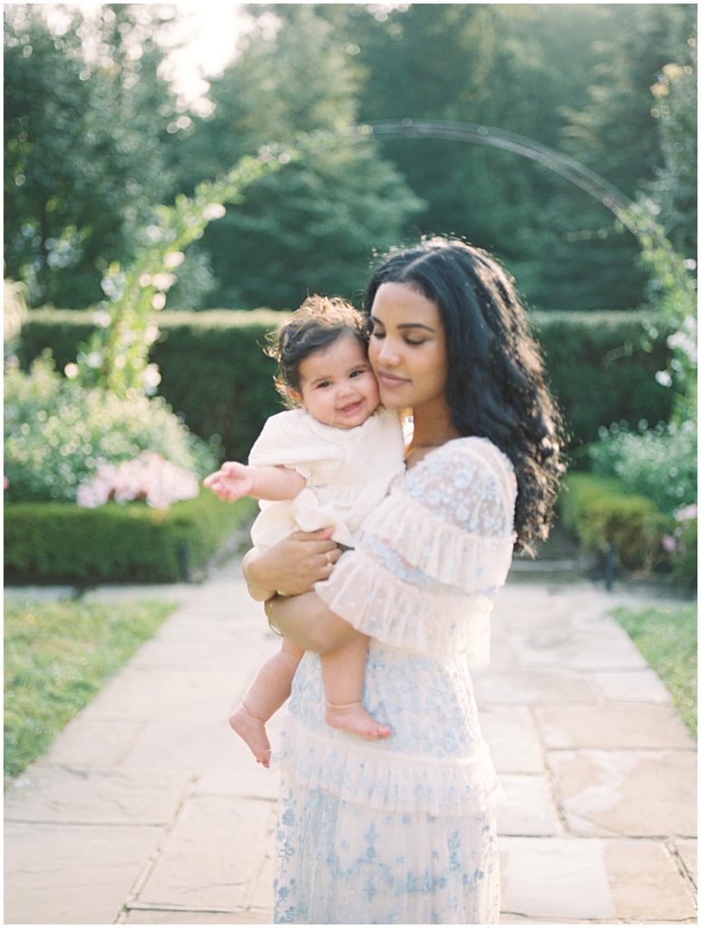 Mother Holds Her Infant Daughter And Smiles During Montgomery County Family Session At Brookside Gardens.