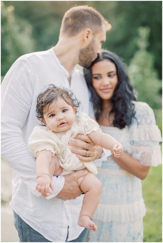 Father Kisses His Wife On The Head As They Hold Their Infant Daughter.