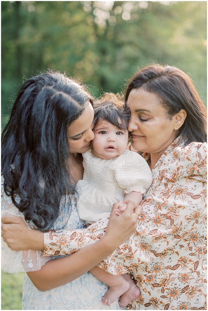 Mother And Grandmother Kiss Baby Girl On Cheek.