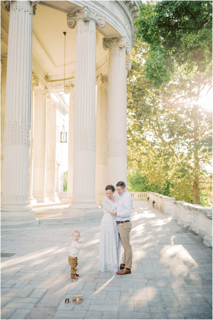 Mother And Father Wrap Arms Around Each Other As They Look Down At Toddler Son During Dar Constitution Hall Photos For Family Session.