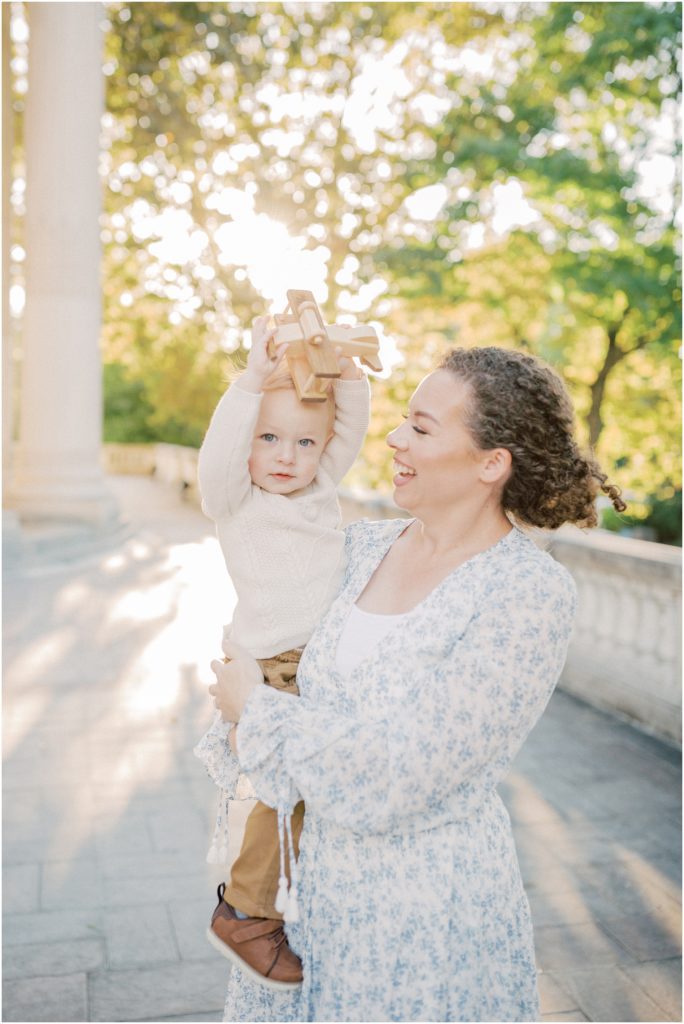 Mother Holds Little Boy With Wooden Plane And Smiles During Dar Constitution Hall Photos For Family Session.