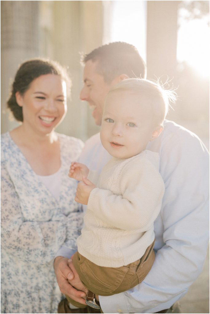 Parents Laugh And Hold Their Son As The Sun Shines On Them During Dar Constitution Hall Photos For Family Session.