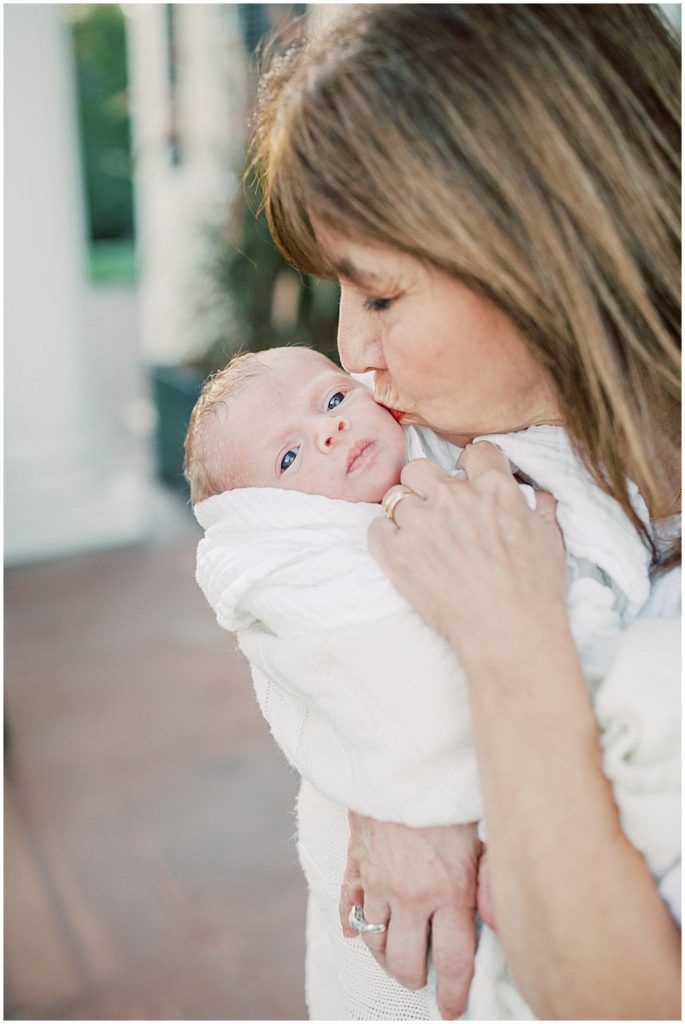 Grandmother Holds Newborn Baby Up And Kisses His Cheek.